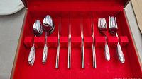 Photo showing cutlery set in wooden box with red felt lining, includes spoons, forks, knives, and chopsticks.