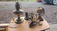 Photo of vintage metal lamp base, stained glass butterfly lamp, owl lamp base, and sun/moon decorative lamp on a wooden table outdoors.