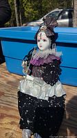 Full view of vintage porcelain clown doll dressed in celestial-themed black, purple, and silver fabric outfit seated outdoors