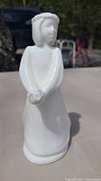 Front view of the white porcelain figurine showing the figure wearing a long dress, floral crown, with hands clasped.