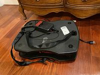 Top view of black vibration platform with control remote and adjustable strap on top.