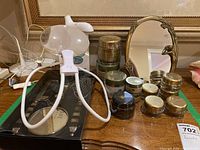 Display of rotary facial cleanser, magnifying glass with stand, jars of beauty creams, and framed mirror on wooden table.