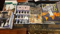 Photograph of four books laid out on a wooden surface including The Times History of the World, Philosophy 100 Essential Thinkers, Wonders of the World, and another book on law and business administration in Canada.