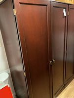 Front view of the wood wardrobe style cabinet with closed doors showing wood grain finish and metal handles.