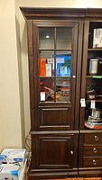Full front view of the tall dark wood cabinet showing the upper glass door with multiple panes and lower solid door.