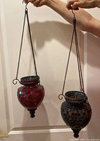 Two mosaic style hanging candle holders, one red and one blue, suspended by black metal chains.