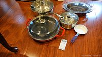 Complete lot shown on wood floor including casserole dish, pots, pan, steamer insert, and small frying pan.