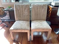Front view of two light-colored upholstered dining chairs with visible stains, placed on wood flooring near a window.