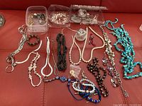 View of assorted costume jewelry including multiple bracelets and necklaces laid out on a red surface.