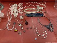 Overview of necklaces and rings laid out on red surface showing different styles and colors of costume jewelry.