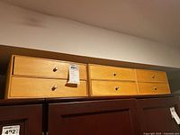Three light wood craft boxes placed on top of darker wood furniture. Each box has two drawers and metal pull knobs.