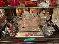 Crystal display cabinet with assorted crystal items: rectangular butter dish, bell, lidded bowls, jar with lid, and multiple candle holders with some red and white candles inserted.