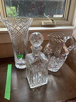 Photo showing 22" tall crystal vase, pitcher, and decanter together on wooden surface near window.