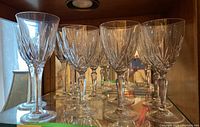 Nine clear crystal wine glasses lined up in a display cabinet showing cut pattern and thick bases