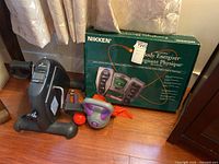 Photo showing mini pedal exerciser, kettlebell, red resistance band, hand grip exerciser, and boxed Nikken Biaxial Body Energizer