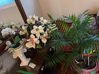 White decorative pedestal with faux magnolia flower arrangement, surrounded by green faux leaves