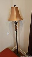 Full view of the metal floor lamp standing against wall with gold tone fabric shade placed on top.