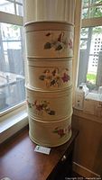 Stack of four round wooden hat boxes painted beige with floral hand paintings.