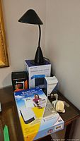 Photo of all items including black desk lamp, Arctos personal space cooler box, SunLite therapy lamp box, solar hand crank camping lantern box, and a small white item on the table.
