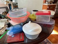 Kitchenware including plastic food storage containers, bowls, and red kitchen scale on a dark table surface.