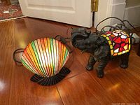 Two decorative lamps on wooden floor; shell-shaped lamp and elephant lamp visible with cords and plug adapters