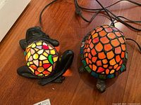 Two animal shaped lamps on a wooden floor, showing frog and turtle with stained glass style light panels and black bases.
