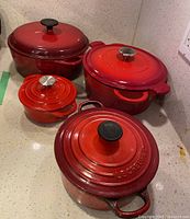 Group of four red enamelled cast iron pots on countertop