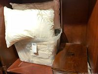 Two white pillows on top of plastic container with linens inside, placed on wooden shelf next to a wooden box.