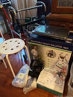 Photo showing adjustable height red rollator with padded seat, white shower stool, bedpan liners and other items on floor.