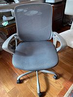 Front view of a gray office chair with mesh backrest and padded seat on caster wheels.