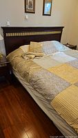 Queen bed with wood headboard, bedding and partial view of mattress on wood floor.
