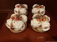 Four teacups with saucers stacked together, showing floral rose patterns and gold trim