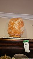 Side view of a large, rough-textured, orange and white Himalayan salt lamp on a wooden base, placed on top of a dark wood piece of furniture.