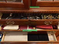 Photo of open drawers showing assorted silverware, cake servers, napkin rings, and folded napkins in storage.