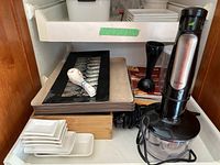 Photo of Braun hand chopper with black and silver design and a transparent container next to Black and Decker immersion blender and assorted white sushi dishes including small plates and square bowls.