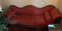 Front view of red damask upholstered wood-framed sofa with two bolster pillows