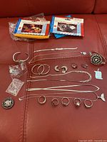 Photo of assorted sterling silver jewelry laid out on a red surface alongside three sealed silver polishing cloths in orange and blue packaging.