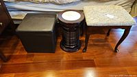 Wide view of three items lined up on wooden floor: black storage box, dark wood swivel stool with white cushioned top, and upholstered wood stool with patterned fabric seat.