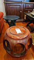 Photo showing two wooden stools: one black folding stool and one carved wood garden stool with circular cutouts.