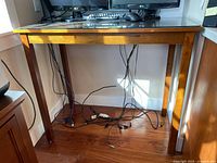 View of wood table with glass top from front, showing the table positioned against a wall, cables underneath