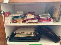 View of stacked placemats, kitchen towels, and napkins folded on a shelf alongside trays.