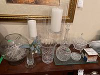 Wide view showing all glass and crystal items: candle holders with white pillar candles, etched glass vases, crystal decanter, covered dish with lid, large etched round bowl with floral carvings and etched glass ornaments inside the bowl.