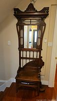 Front view of the vintage wooden hall tree showing mirror, decorative top, spindle back, and wooden seat.