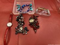 Overall view of watches, beaded jewelry, and transparent coin purse on red surface.