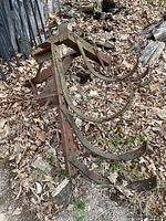 Rusty metal farm plow with curved blades laid on ground covered with leaves and wood debris