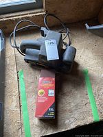 FMT electric belt sander placed on a wood surface with power cord visible, including a ticket with auction number.