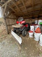 Full view of red Honda Foreman ES ATV under shelter showing front-mounted snow plow, wooden box on front rack, rear cargo rack and surrounding buckets.