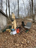 Full view of lot showing various garden tools, wooden planks, gas cans, sprayer, chair, and car jack in outdoor setting.