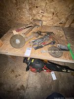 Photo showing multiple miscellaneous hand tools including a wooden-handled hammer, hand auger, spirit levels, plumb bob, and a chainsaw below the shelf.
