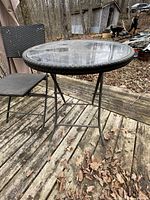 Round glass-top bistro table with black metal frame on outdoor wooden deck.